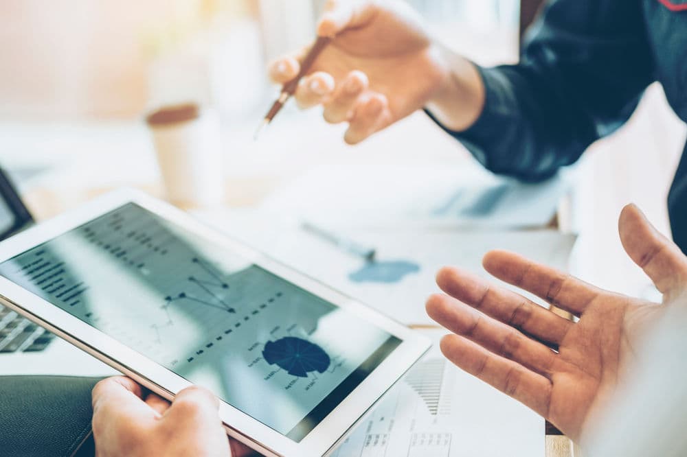 Person analyzing data charts on a tablet during a business meeting with hands gesturing.
